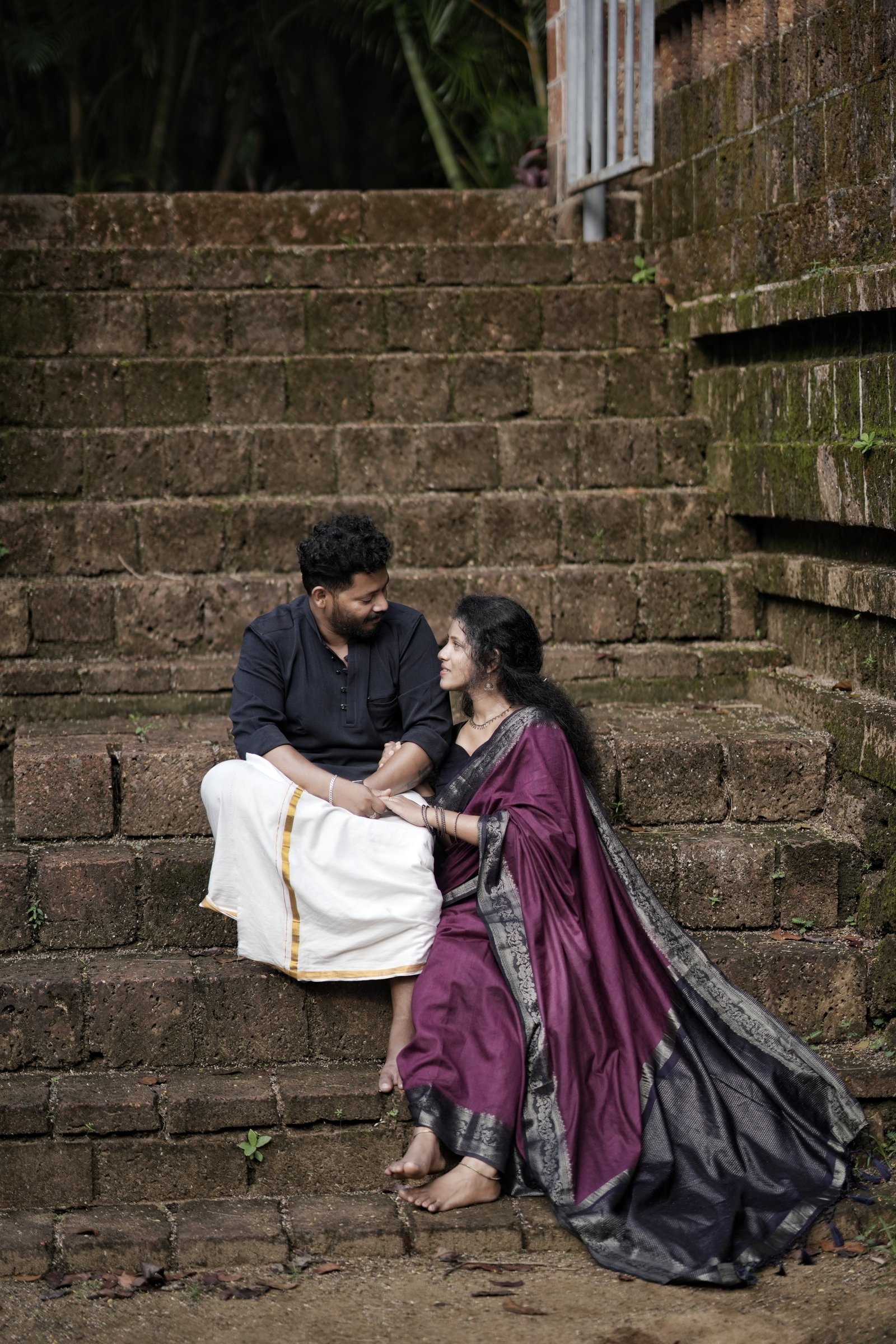 Rahul and Sruthy sitting together holding hands on rustic stone steps